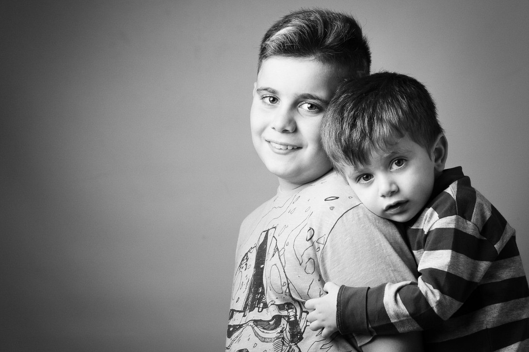 Due bambini sorridenti in una fotografia in bianco e nero, il più grande abbraccia il più piccolo che si appoggia sulla sua schiena.