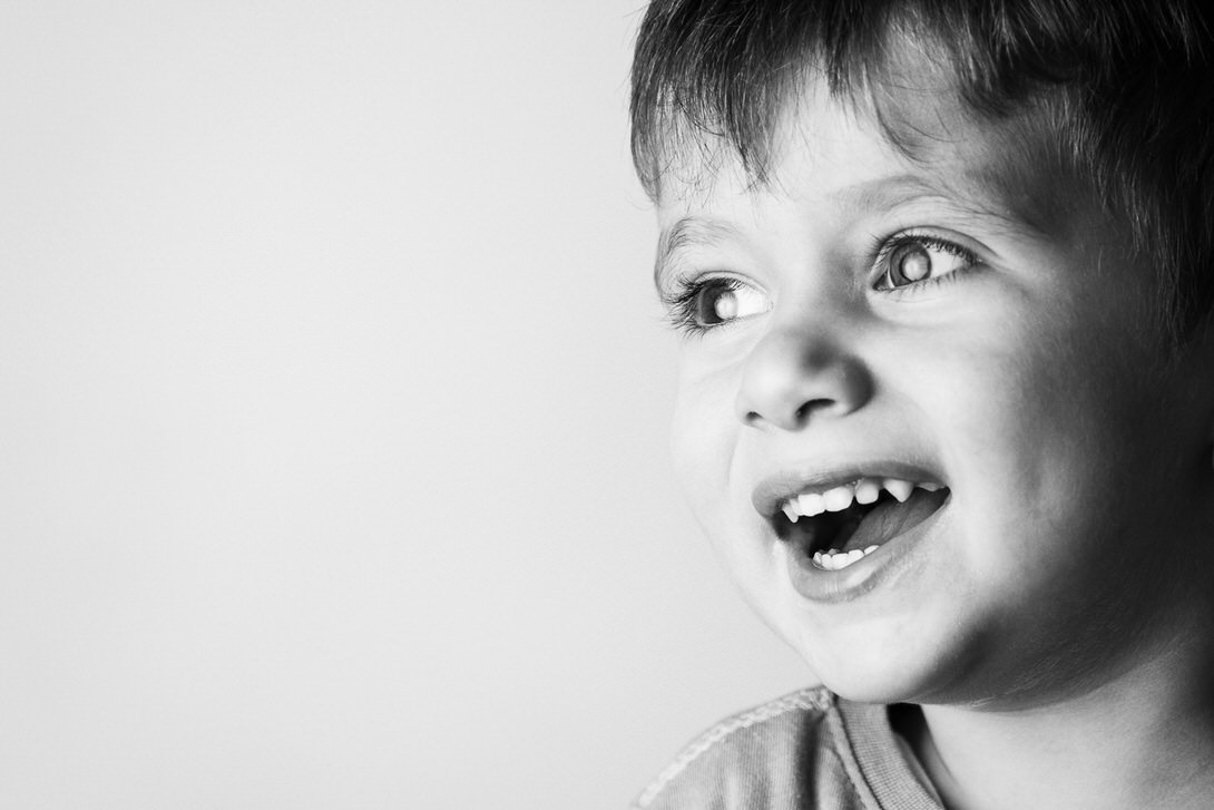 Bambino sorridente con occhi luminosi e capelli corti, in un'immagine in bianco e nero, che trasmette gioia e spontaneità.