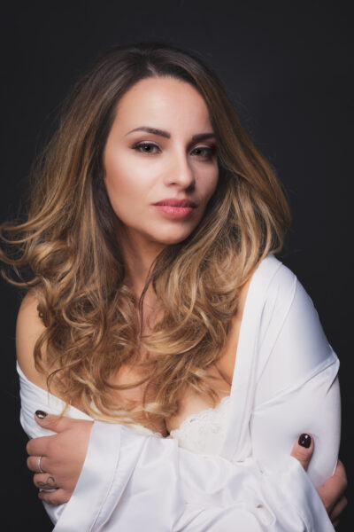 Ritratto di donna con capelli lunghi e mossi, trucco naturale, indossando una camicia bianca, su sfondo scuro.