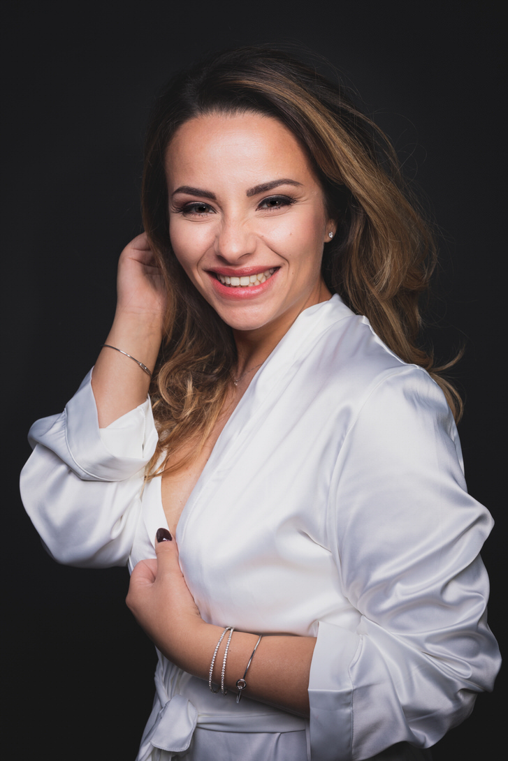 Ritratto di una donna sorridente con capelli ondulati, che indossa una camicia bianca, su sfondo scuro. L'immagine trasmette gioia e confidenza.