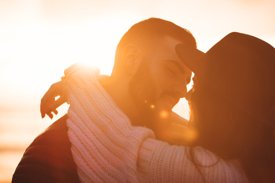 Coppia innamorata che si abbraccia al tramonto, con luce dorata che illumina i loro volti e crea un'atmosfera romantica.