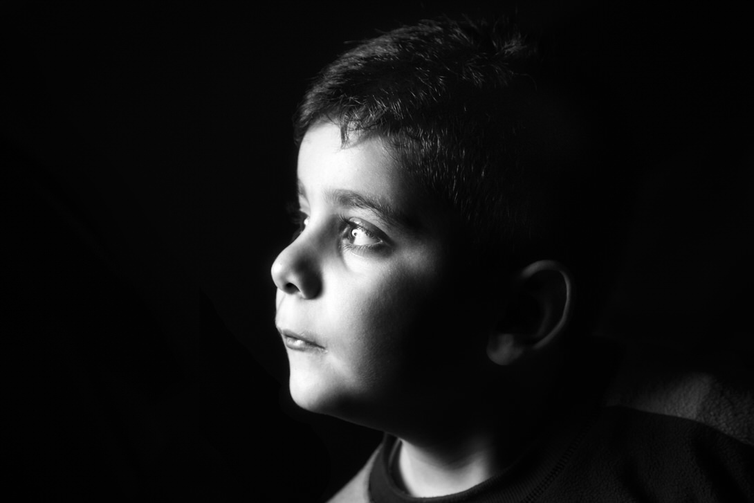 Gabriele Ritratto in bianco e nero di un bambino con uno sguardo pensieroso, illuminato da una luce soft che mette in risalto i suoi tratti.