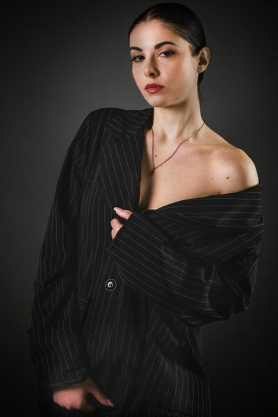 Modella con giacca oversize a righe nere, in posa seria su sfondo scuro, evidenziando un look elegante e sofisticato.