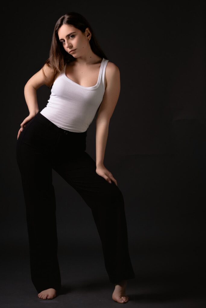 Ritratto fotografico in studio dal progetto “Senza far rumore”: figura femminile su fondo neutro scuro, luce laterale morbida che scolpisce volto e corpo, postura controllata e tensione trattenuta, espressione essenziale e non costruita, fotografia minimalista basata su presenza, sottrazione e controllo del gesto.