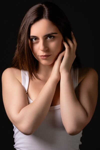 Ritratto fotografico in studio dal progetto “Senza far rumore”: figura femminile su fondo neutro scuro, luce laterale morbida che scolpisce volto e corpo, postura controllata e tensione trattenuta, espressione essenziale e non costruita, fotografia minimalista basata su presenza, sottrazione e controllo del gesto.