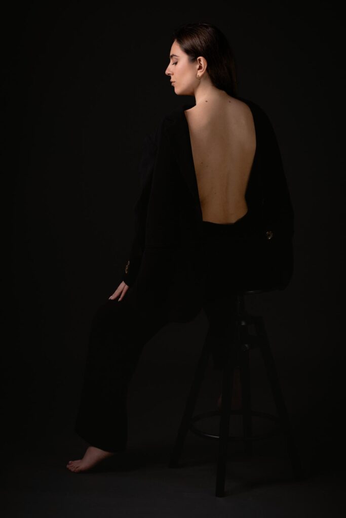 Ritratto fotografico in studio dal progetto “Senza far rumore”: figura femminile su fondo neutro scuro, luce laterale morbida che scolpisce volto e corpo, postura controllata e tensione trattenuta, espressione essenziale e non costruita, fotografia minimalista basata su presenza, sottrazione e controllo del gesto.