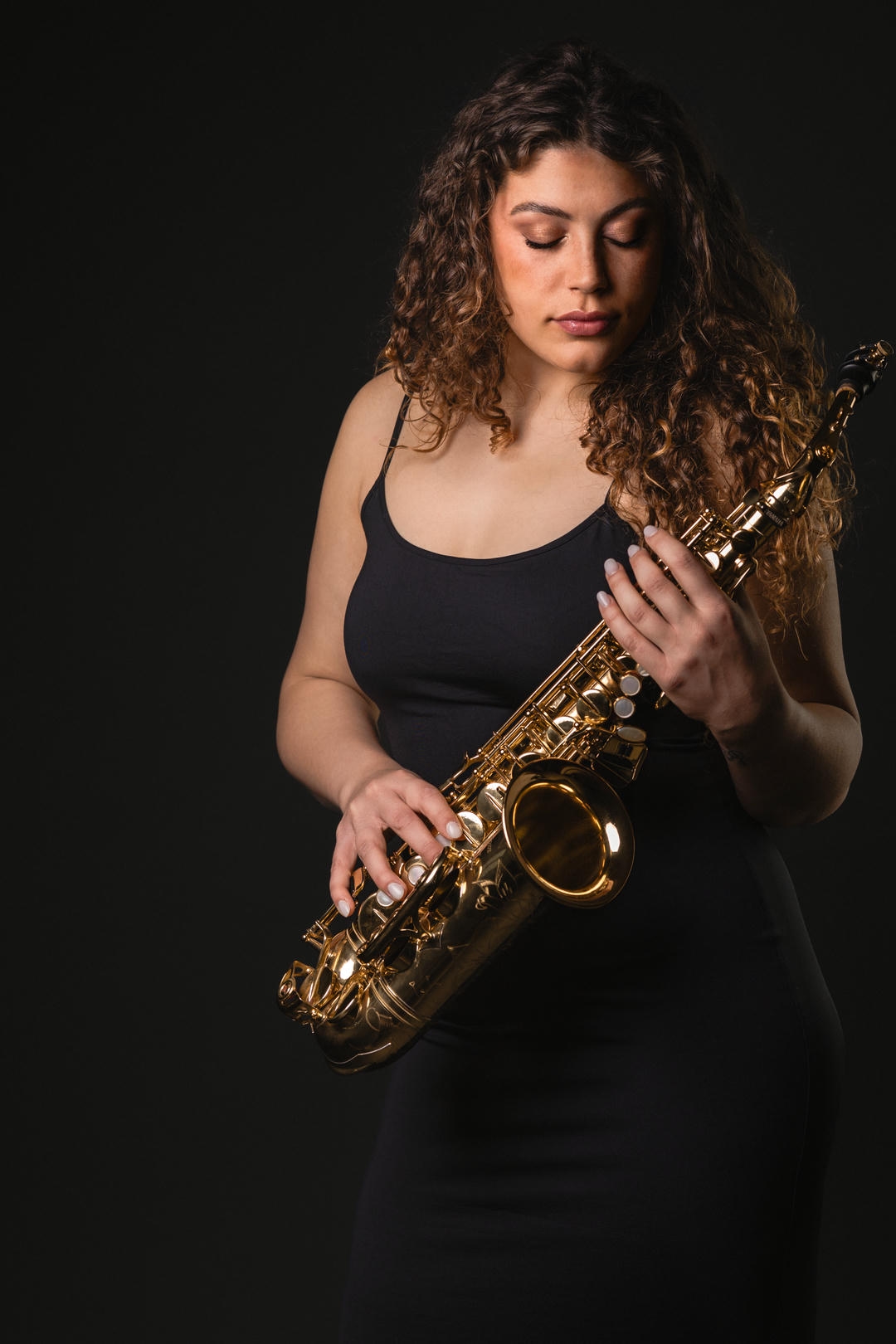 Golden Silence – Appunti su luce, ottone e ritratto Ritratto editoriale di una donna in abito nero che guarda un sax dorato, illuminata lateralmente su fondo scuro.